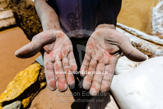 The hands of a laborer working the terraced pond walls in an ancient Inca salt mine. Maras, Peru.