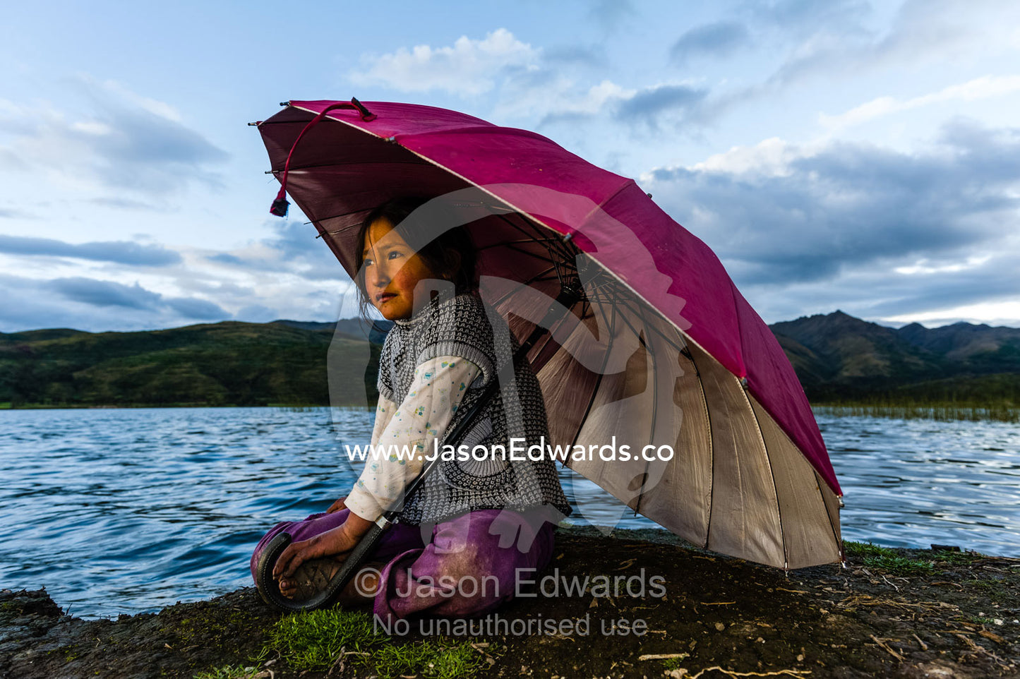 A girl sits under an umbrella on a lake shore in the mountains. Maras, Peru.