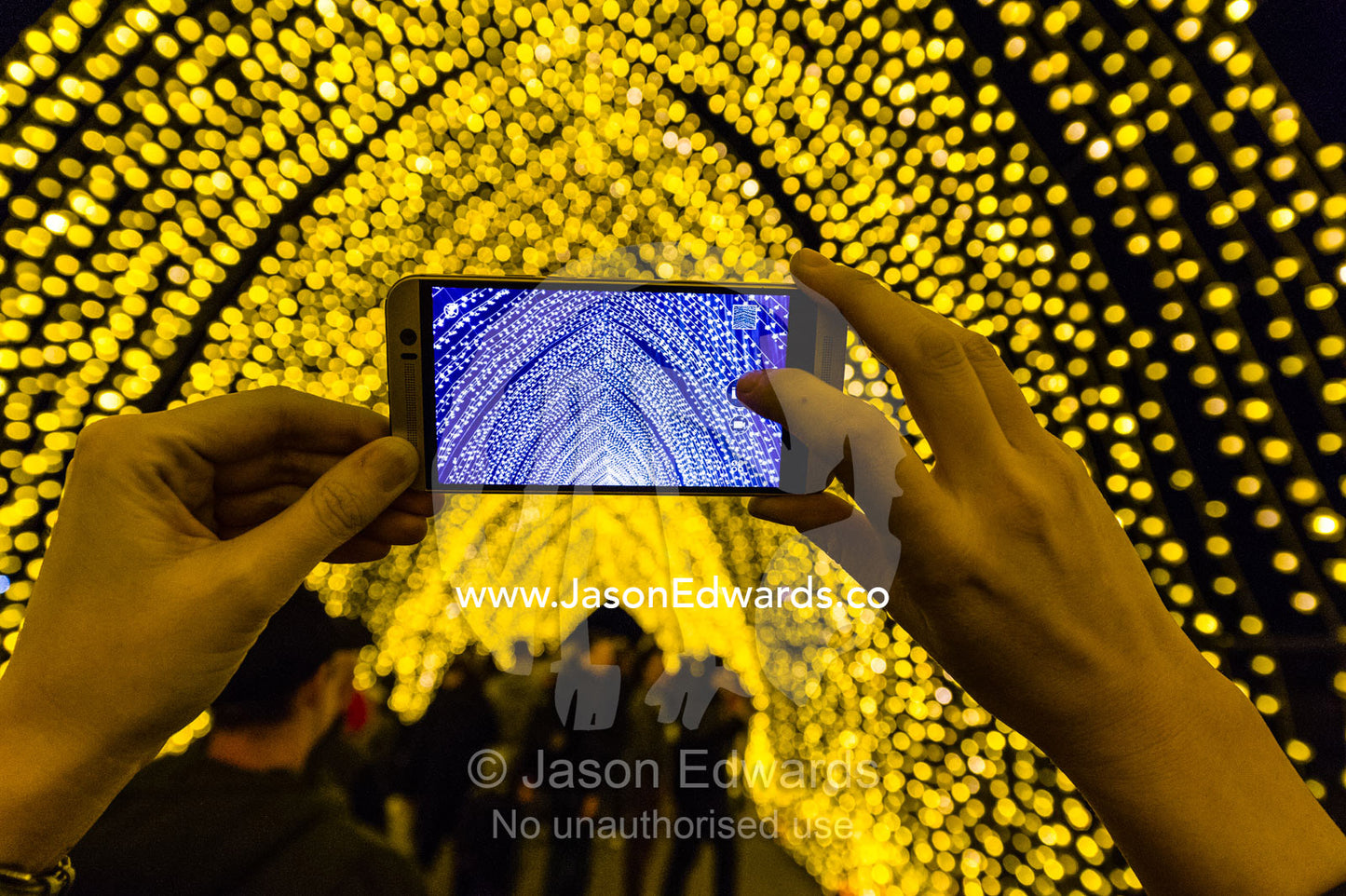 A person photographs an archway of lights on a cell phone in the Cathedral of Light. Sydney, New South Wales, Australia.