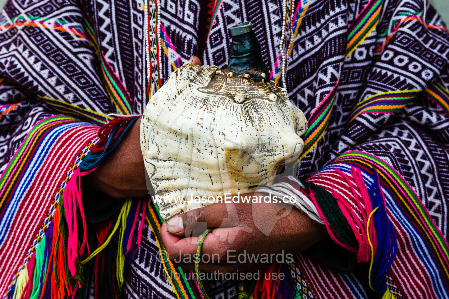 An Amaru man wearing a colourful handwoven poncho holding a shell horn. Pisac, Peru.