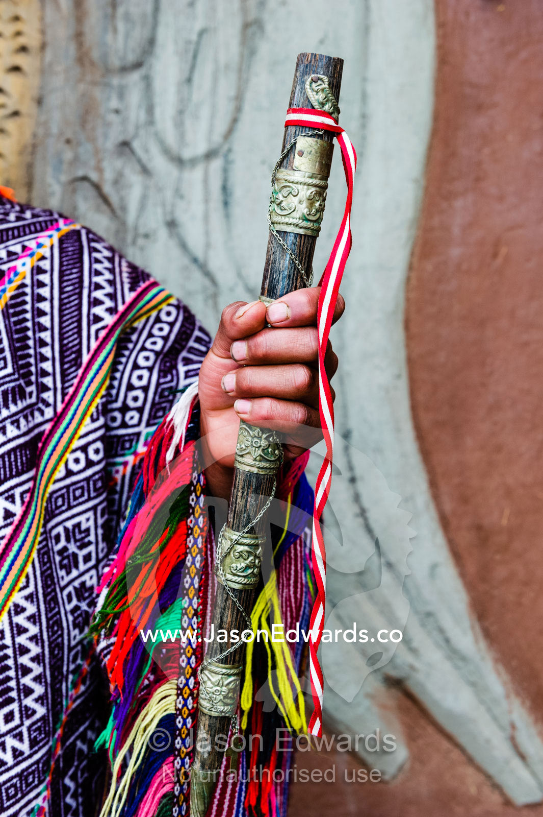 An Amaru man wearing a colourful handwoven poncho holding a brass and timber flute. Pisac, Peru.