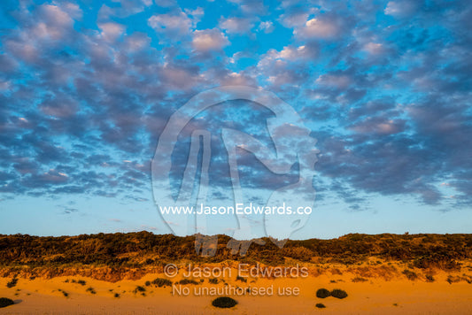 A cluster of clouds gather over a sand dune at sunset. Victoria, Australia.