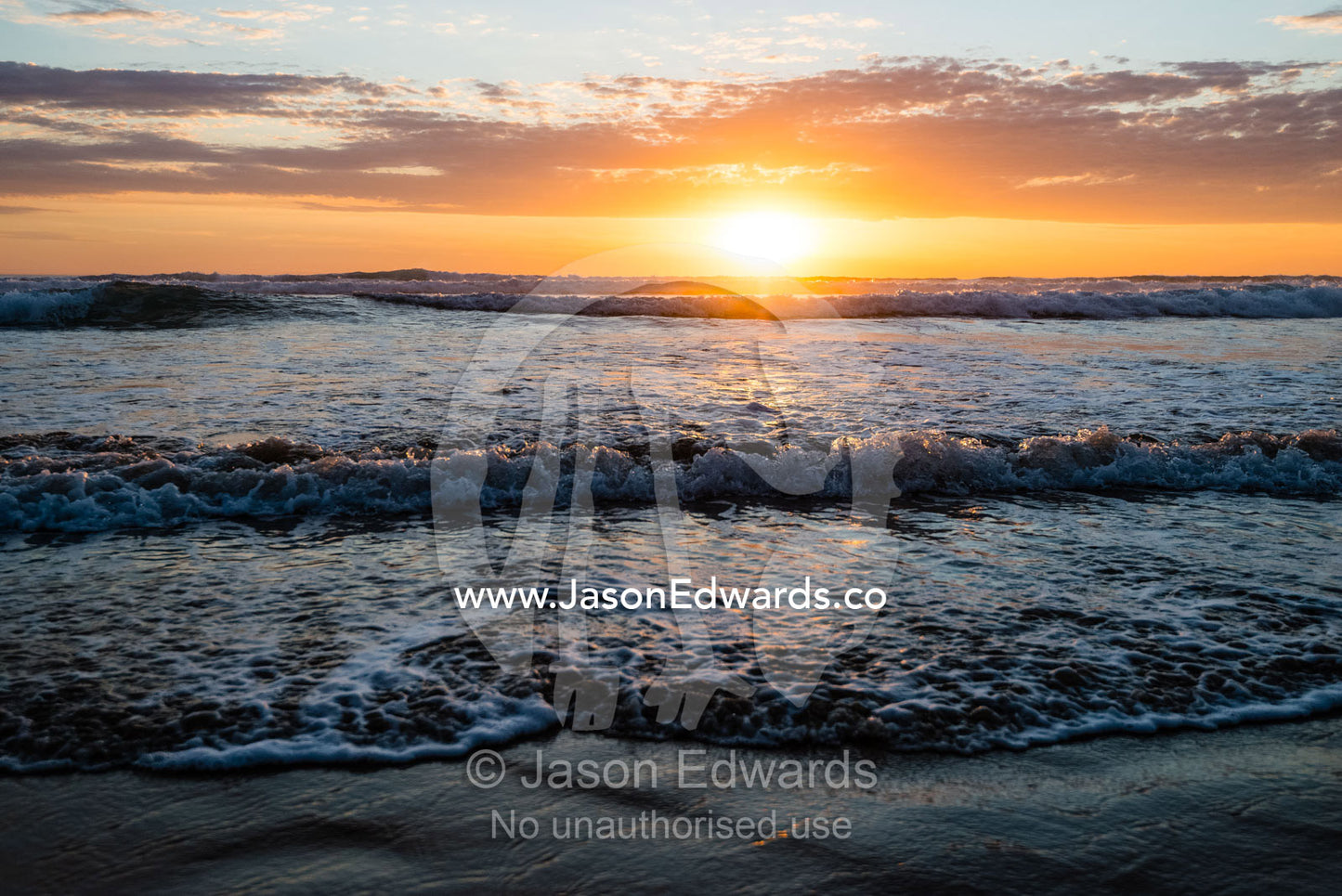 An incoming tide pushes waves onto a beach at sunset. Victoria, Australia.