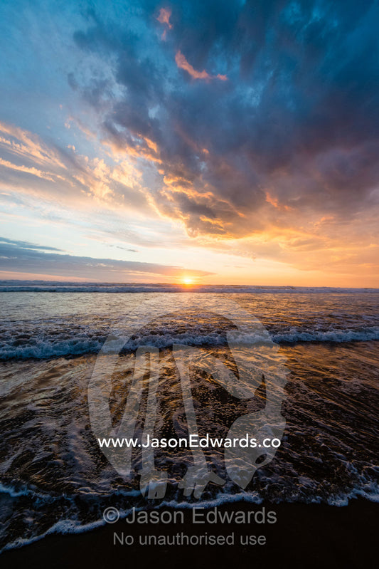 Beneath a storm front an incoming tide pushes waves onto a beach at sunset. Victoria, Australia.