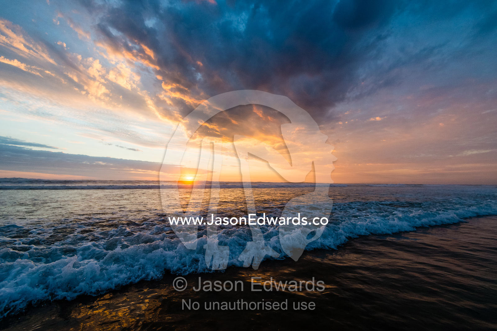 Beneath a storm front an incoming tide pushes waves onto a beach at sunset. Victoria, Australia.