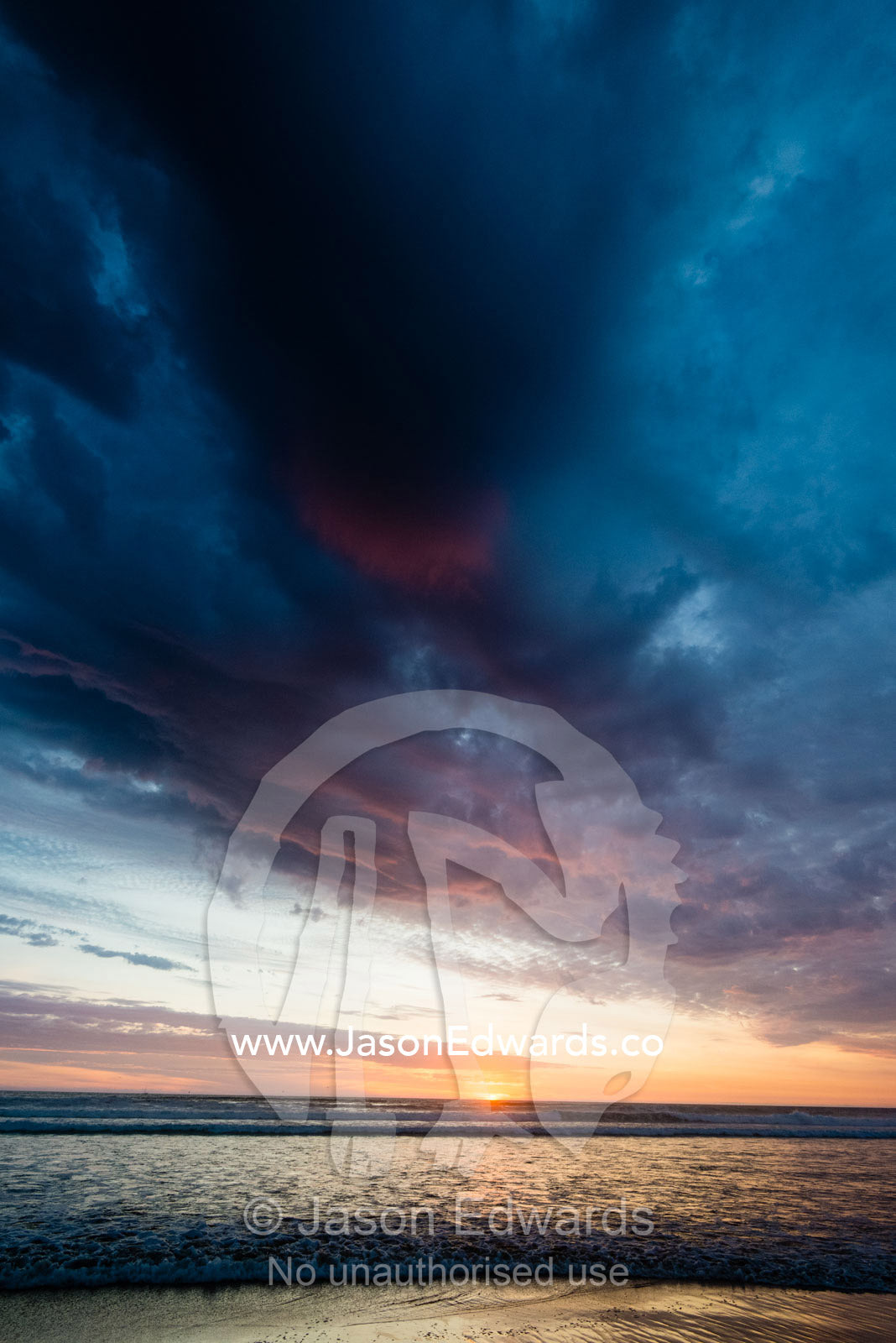 Beneath a storm front an incoming tide pushes waves onto a beach at sunset. Victoria, Australia.