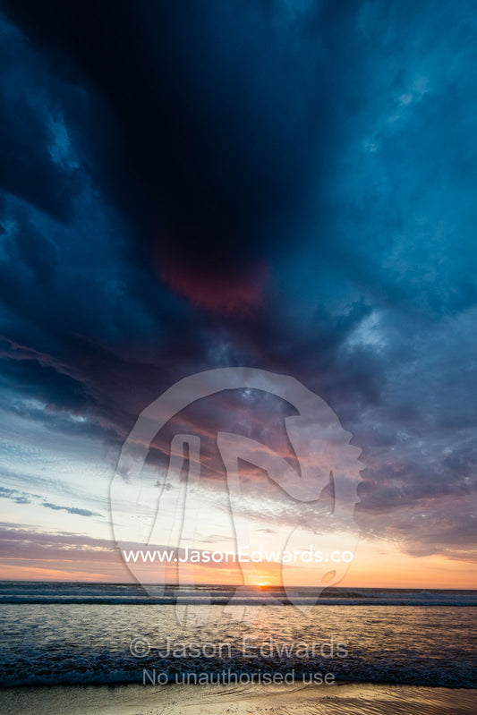 Beneath a storm front an incoming tide pushes waves onto a beach at sunset. Victoria, Australia.