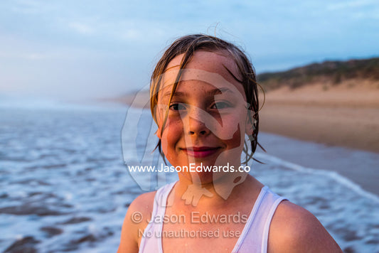 A boy standing in the shallows as the tide comes in at sunset. Victoria, Australia.