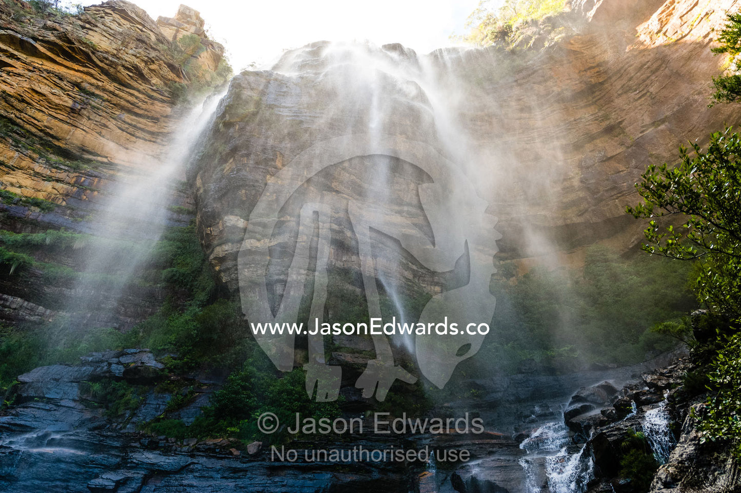 A curtain of mist and water cascades from a waterfall on a sandstone cliff. Blue Mountains National Park, New South Wales, Australia.