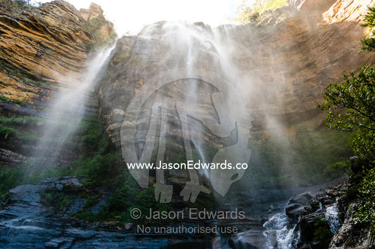 A curtain of mist and water cascades from a waterfall on a sandstone cliff. Blue Mountains National Park, New South Wales, Australia.