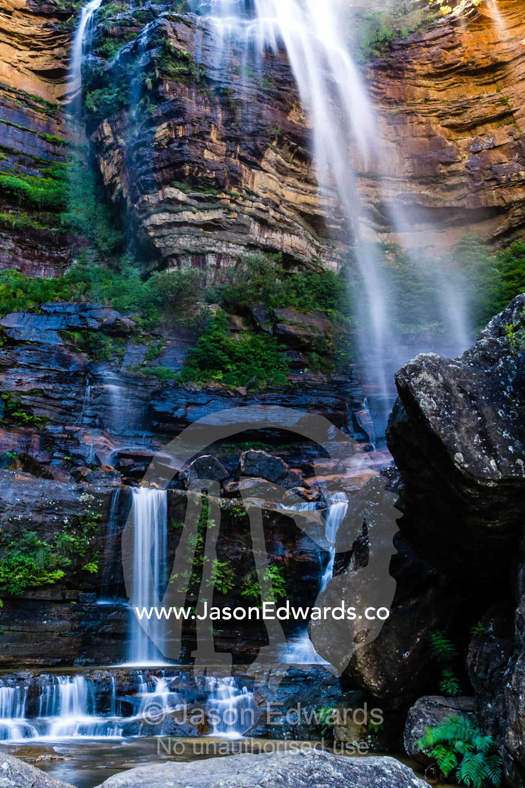 A curtain of mist and waterfalls cascades from a sandstone cliff into rock pools. Blue Mountains National Park, New South Wales, Australia.