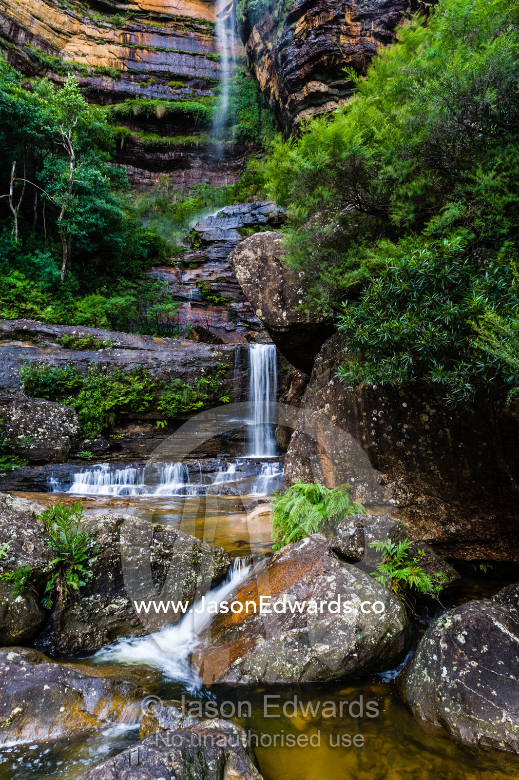 A curtain of mist and waterfalls cascades from a sandstone cliff into rock pools. Blue Mountains National Park, New South Wales, Australia.