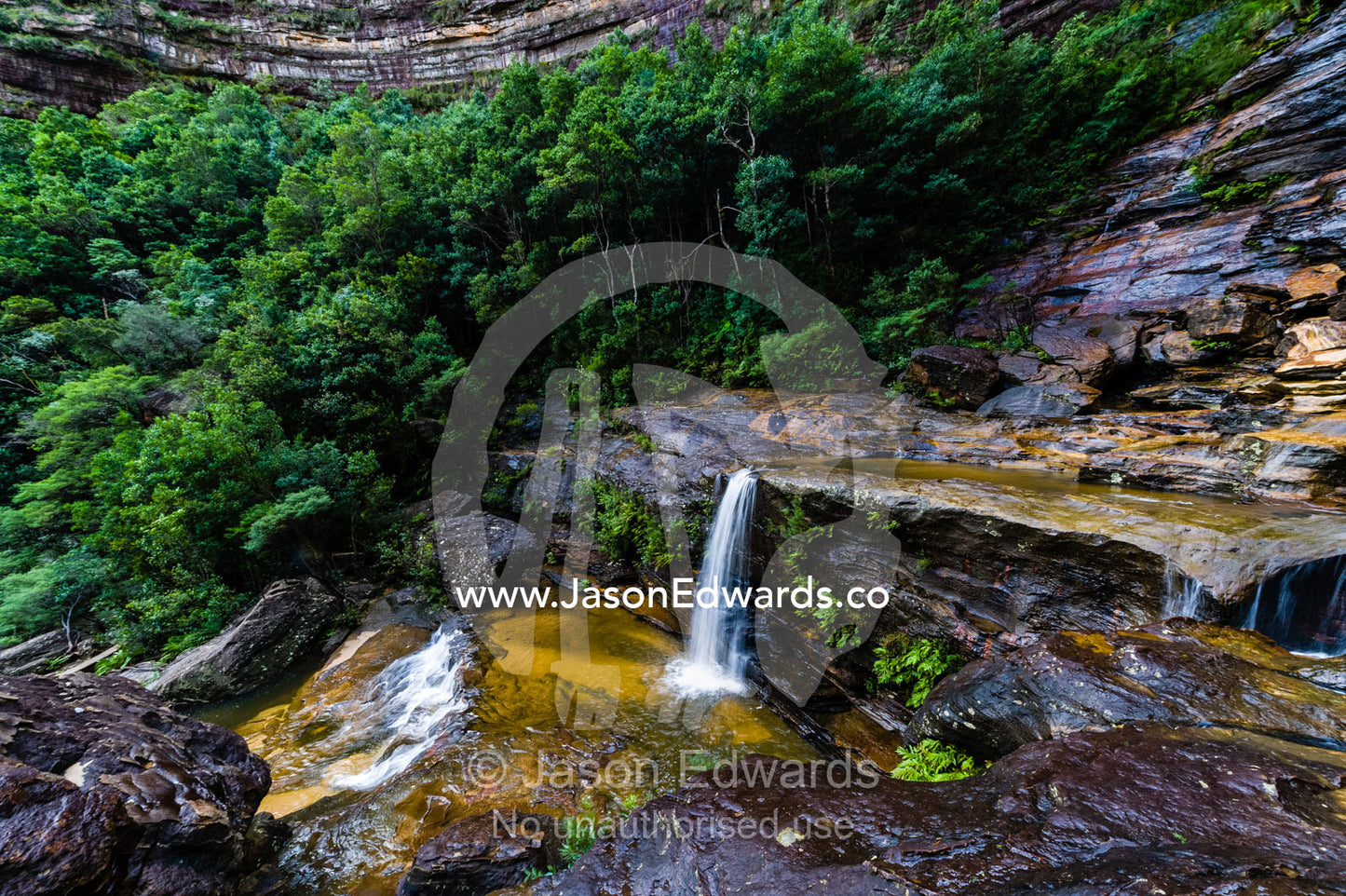A curtain of mist and waterfalls cascades from a sandstone cliff into rock pools. Blue Mountains National Park, New South Wales, Australia.