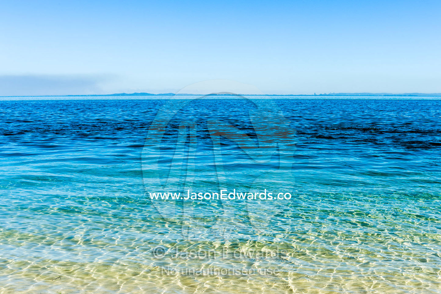 Turquoise seas lap onto the shore of a deserted island. Queensland, Australia.