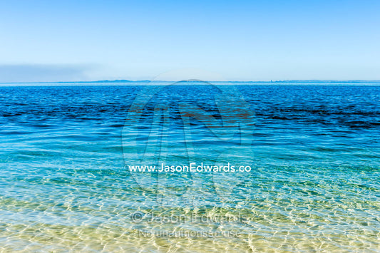 Turquoise seas lap onto the shore of a deserted island. Queensland, Australia.