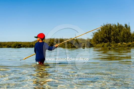 An Aboriginal boy uses a long barbed spear to hunt for stingrays in the shallows of a lagoon. Queensland, Australia.