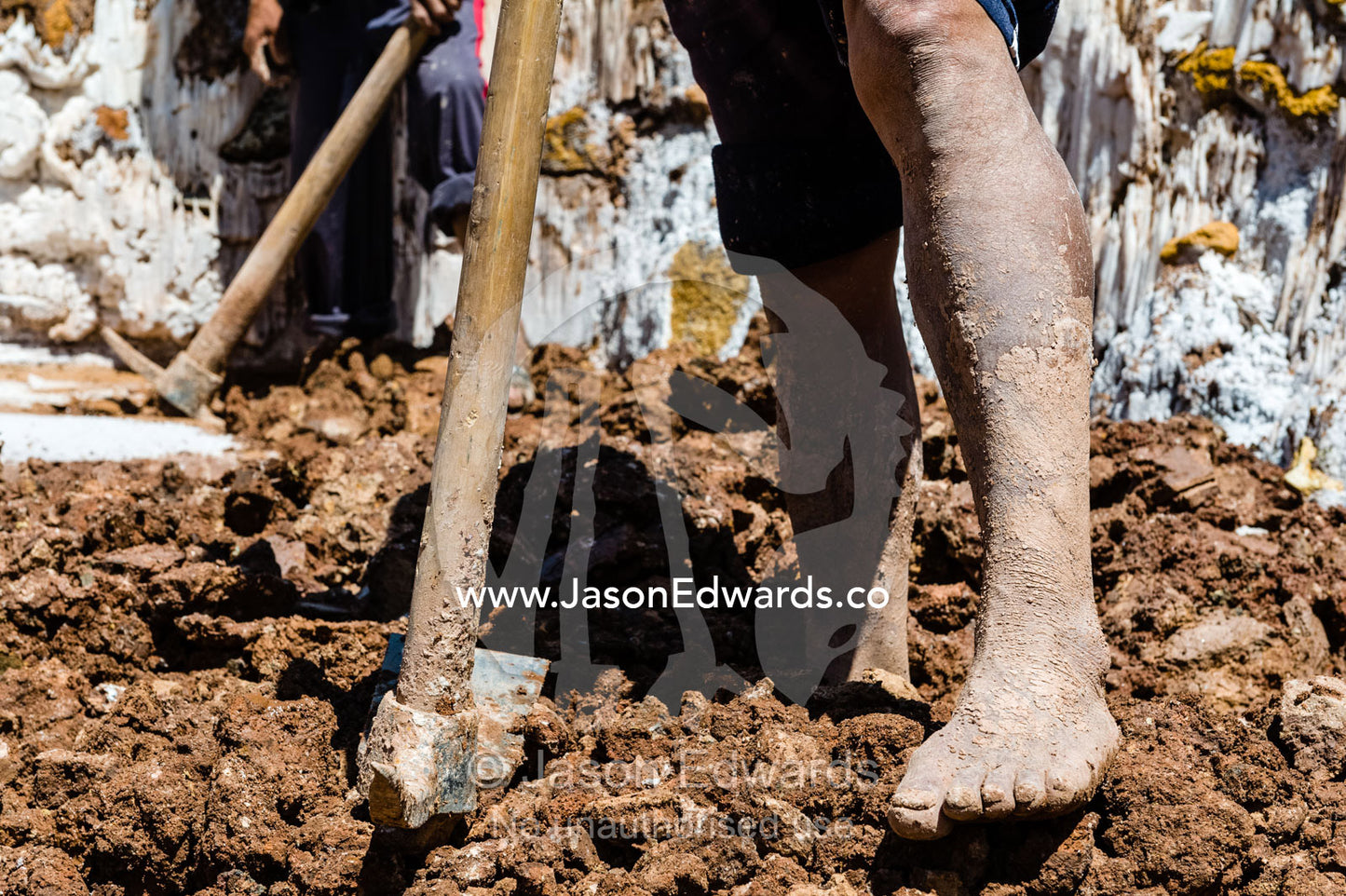 A labourer uses a spade to make salt evaporation ponds in an ancient Inca salt mine. Maras, Peru.