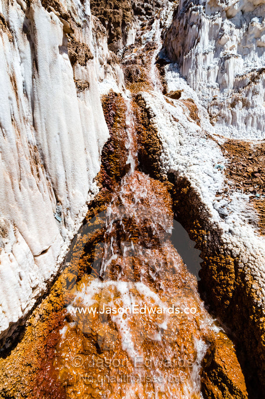 Salty spring water flows down channels into terraced evaporation ponds in an Inca salt mine. Maras, Peru.