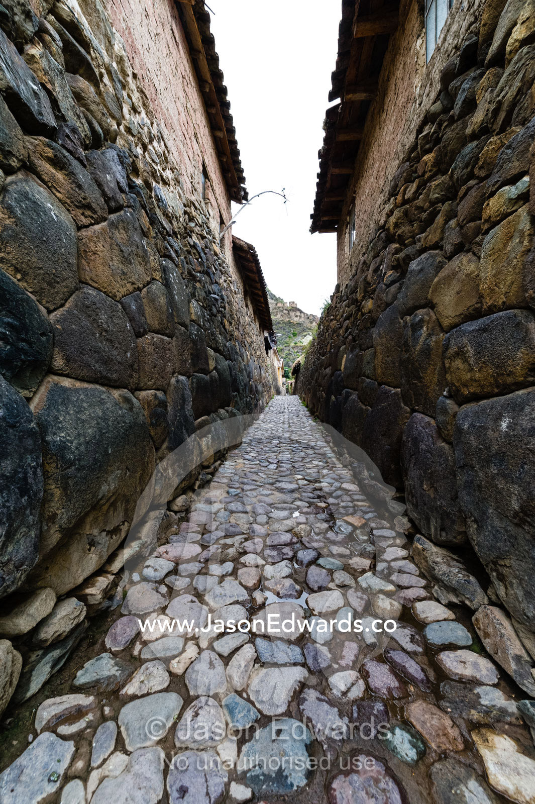 A village lane paved with stones and lined with high Inca dry-stone walls. Ollantaytambo, Peru.