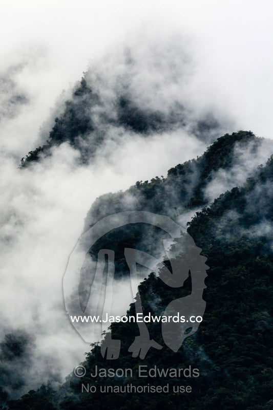 Storm clouds engulf the steep forested slopes and jagged mountain peaks of the Andes. Peru.