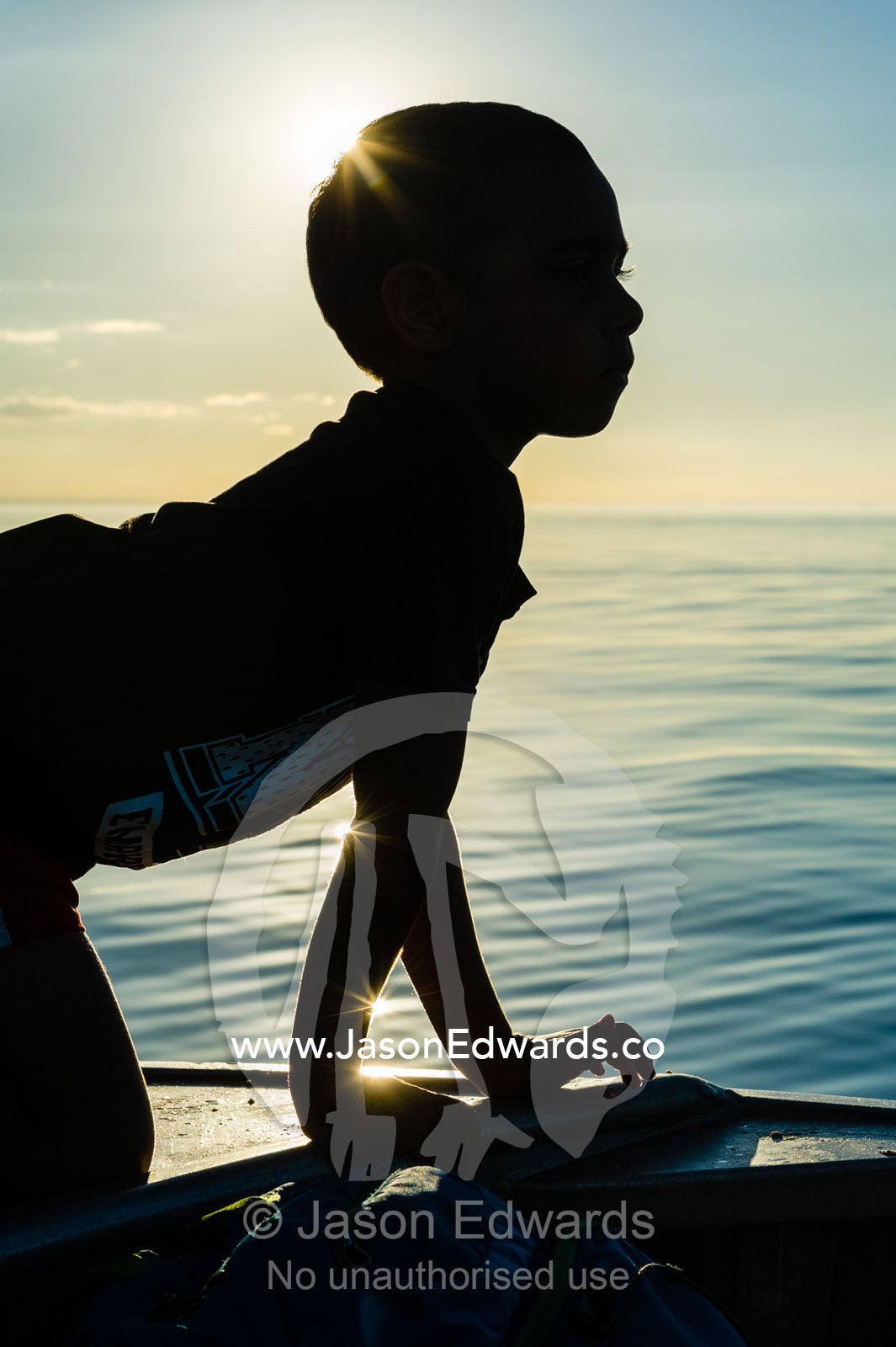 The silhouette of an Aboriginal boy scanning the ocean horizon at sunset. Queensland, Australia.