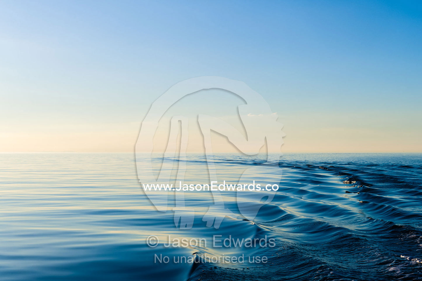 Boat wake ripples across a dead calm ocean surface at twilight. Queensland, Australia.