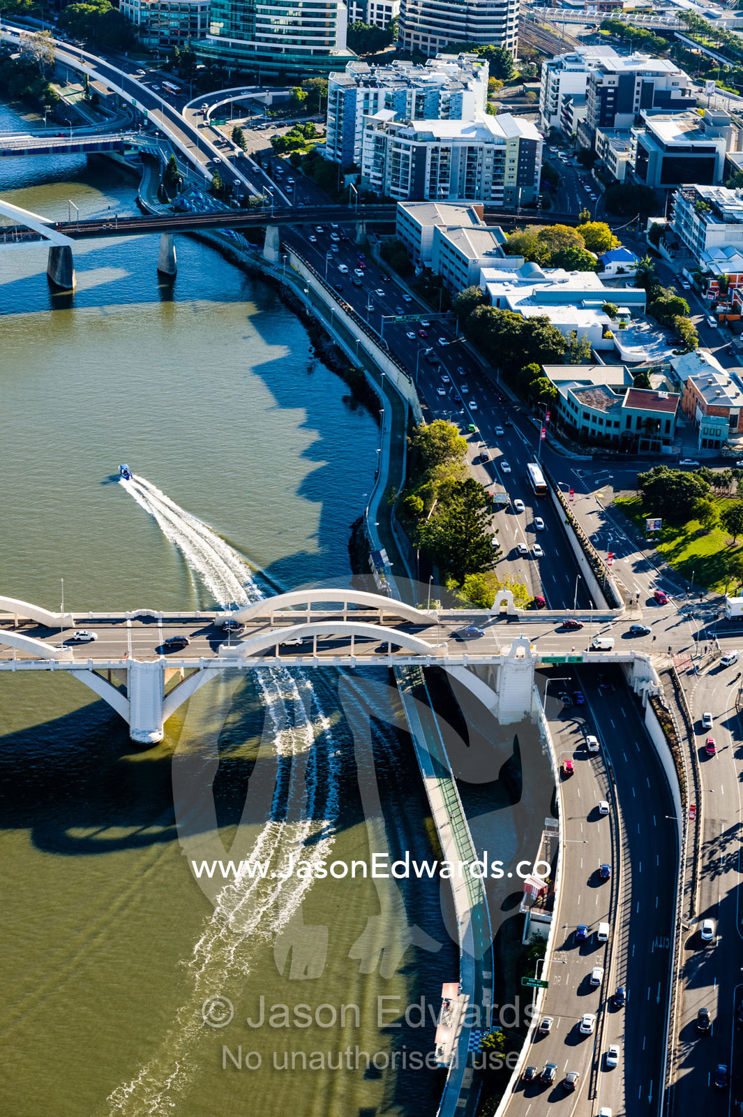 A speedboat passes beneath a river bridge leaving traffic on a freeway behind. Brisbane, Queensland, Australia.