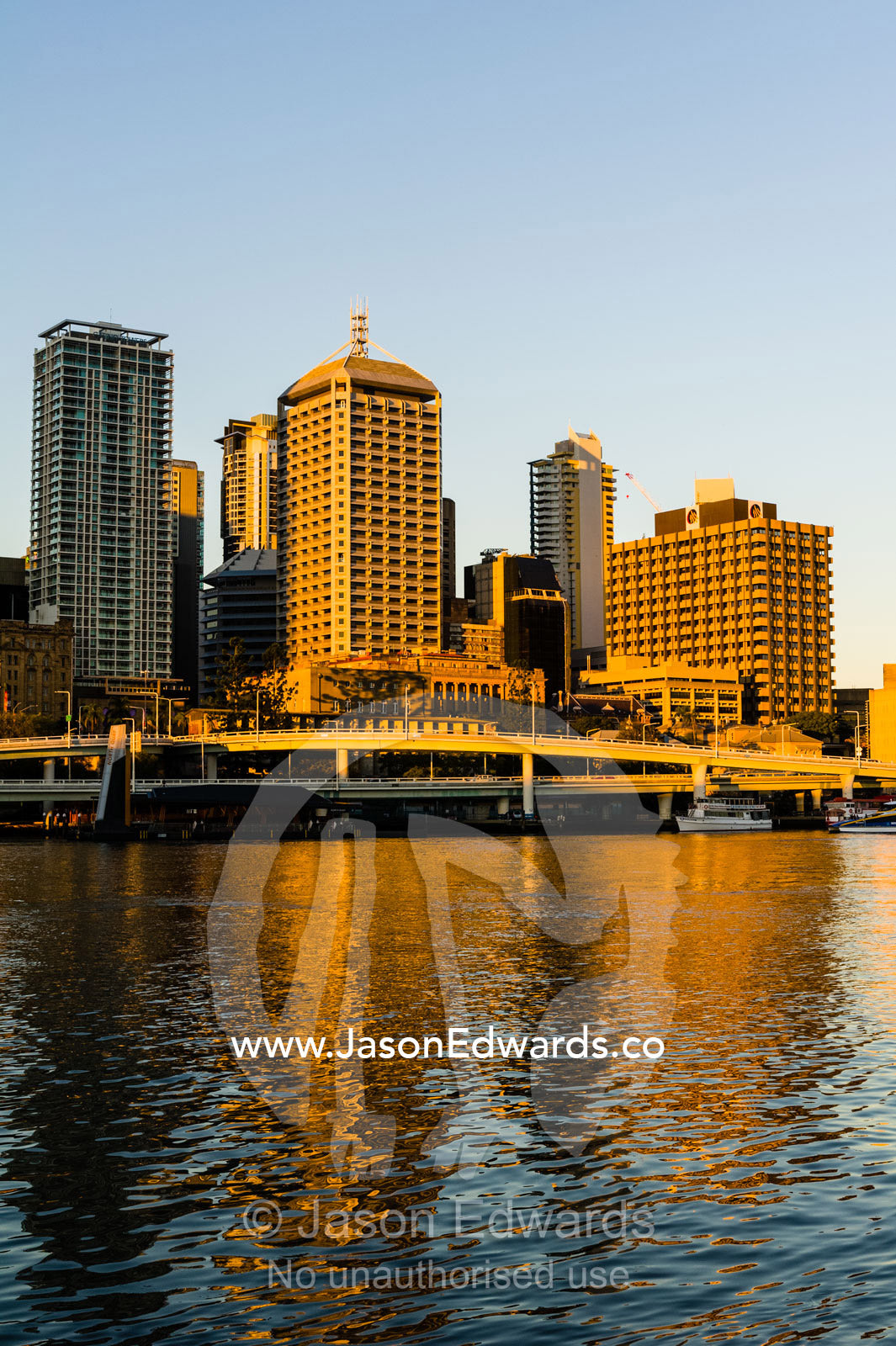 A freeway overpass runs along a river beneath an office building skyline. Brisbane, Queensland, Australia.