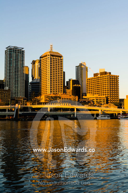 A freeway overpass runs along a river beneath an office building skyline. Brisbane, Queensland, Australia.