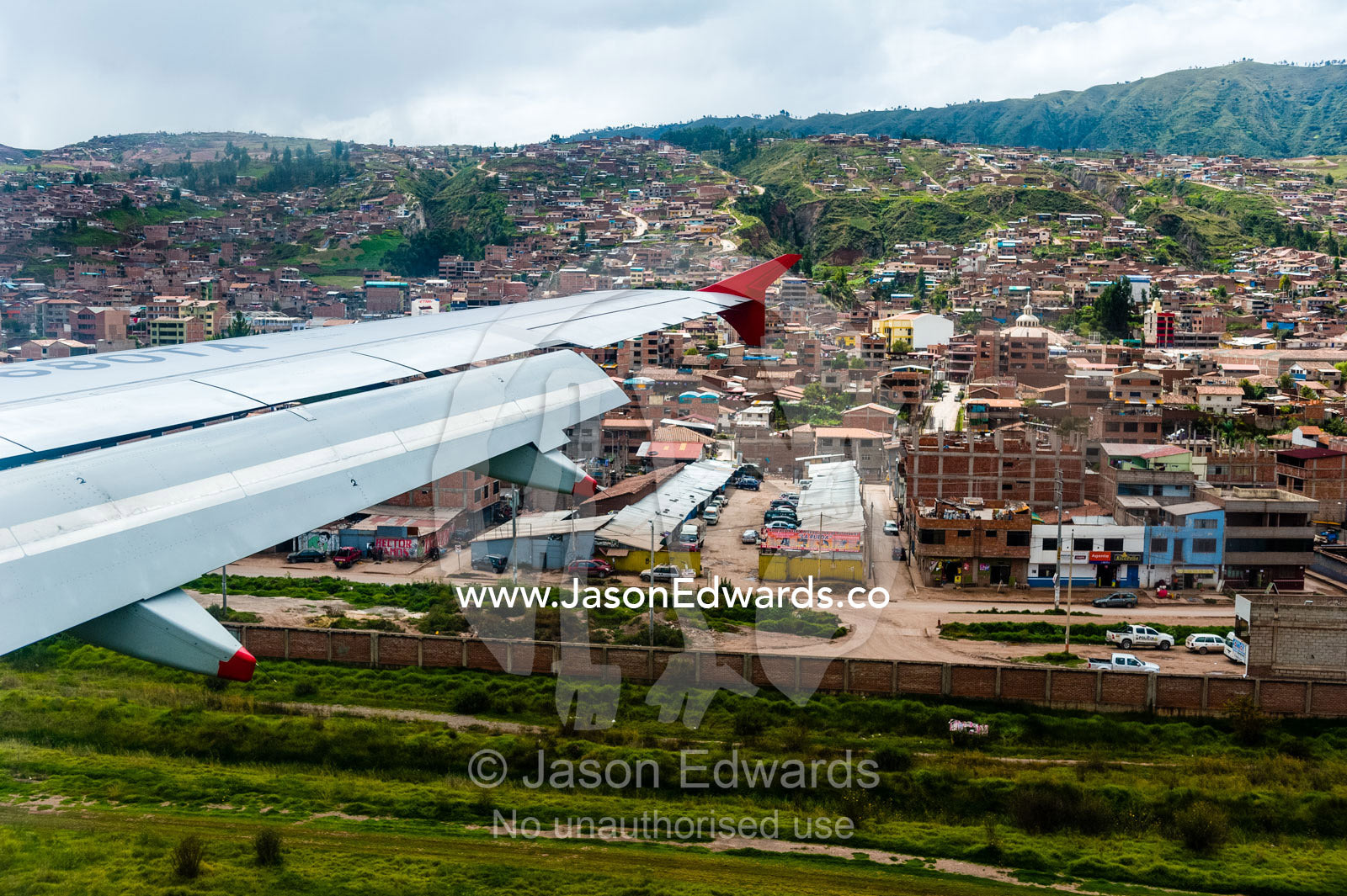 A plane wing flying over an airport and city suburbs in the Andes mountains. Cusco, Peru.