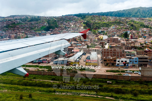 A plane wing flying over an airport and city suburbs in the Andes mountains. Cusco, Peru.