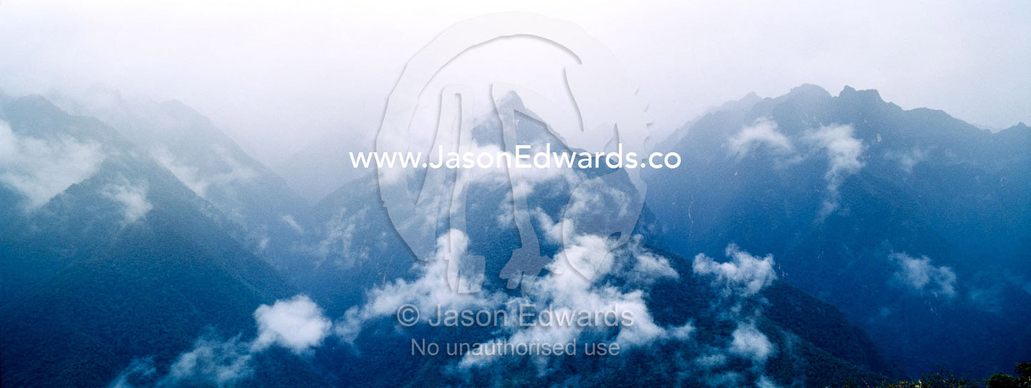 Storm clouds engulf the steep forested slopes and jagged mountain peaks of the Andes. Peru.