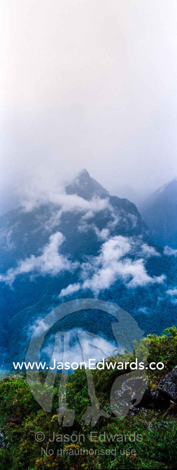 Storm clouds engulf the steep forested slopes and jagged mountain peaks of the Andes. Peru.
