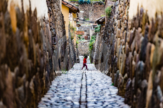 A small child walks through the ancient Inca cobblestone lanes of a Andes town. Sacred Valley, Ollantaytambo, Urubamba, Peru