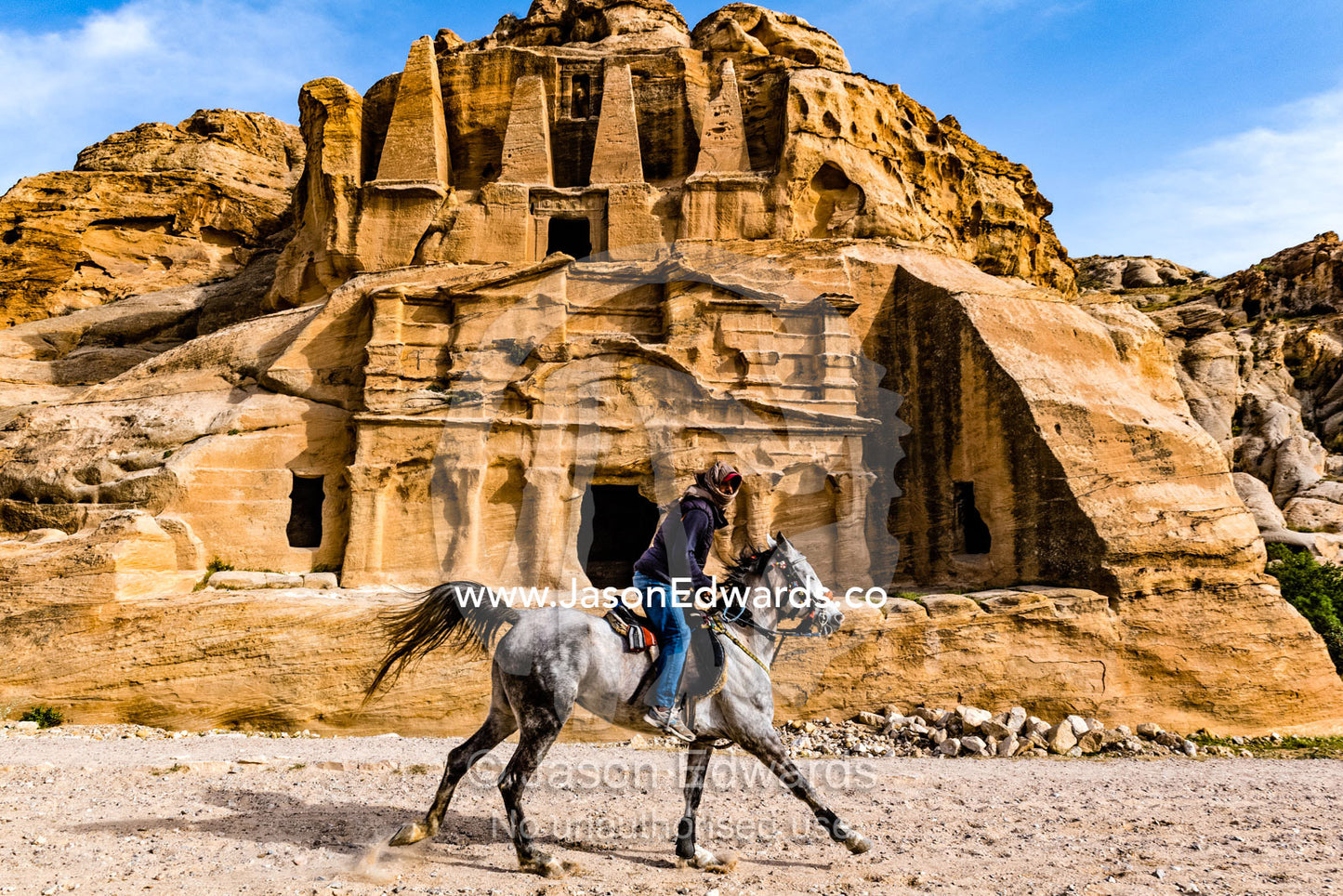 A Bedouin man galloping on a horse past the ancient ruins of the Obelisk Tomb, above, and Bab as-Siq Triclinium, below, rock-cut architecture, 1st century AD. Petra, The Lost City of Petra, Jordan