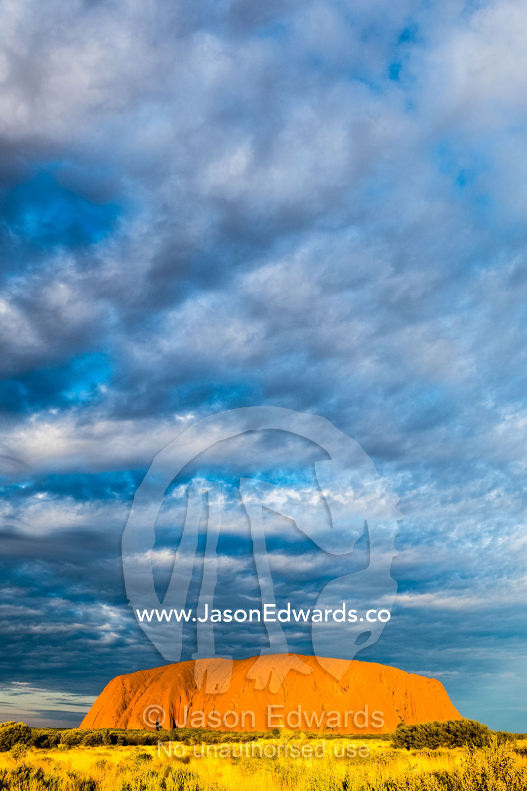 Clouds fill the vast desert sky over the ochre face of Uluru. Uluru-Kata Tjuta National Park, Northern Territory, Australia