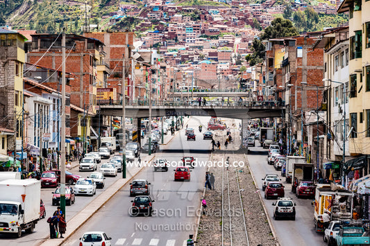 Traffic congestion and train lines running along a main road in an Andean city. Cusco, Cusco Region, Peru