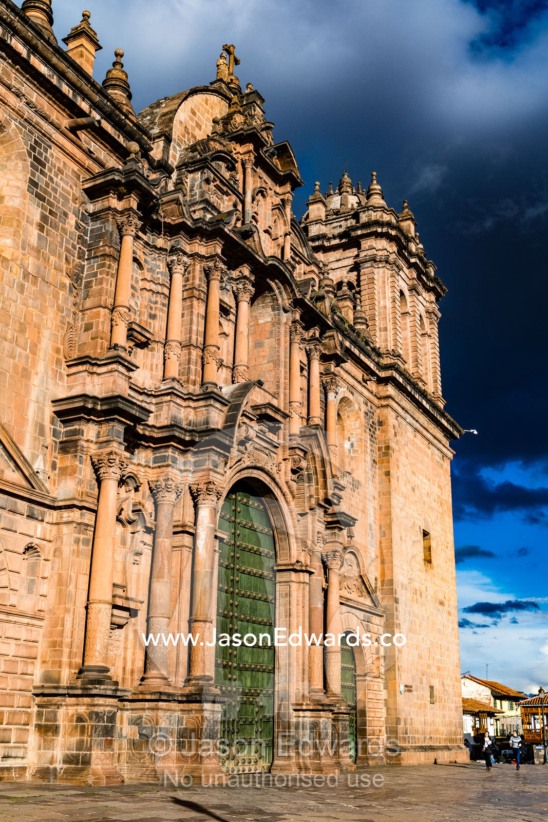 The imposing stone facade of a large Catholic church beneath a storm cloud. Cusco, Cusco Region, Peru
