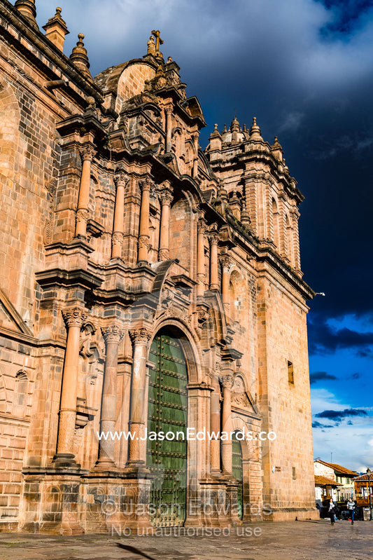 The imposing stone facade of a large Catholic church beneath a storm cloud. Cusco, Cusco Region, Peru