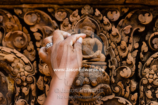 A person touches a sandstone relief carving of Buddha in a temple while offering a prayer. Phnom Dei, Banteay Srei, Banteay Srey, Cambodia
