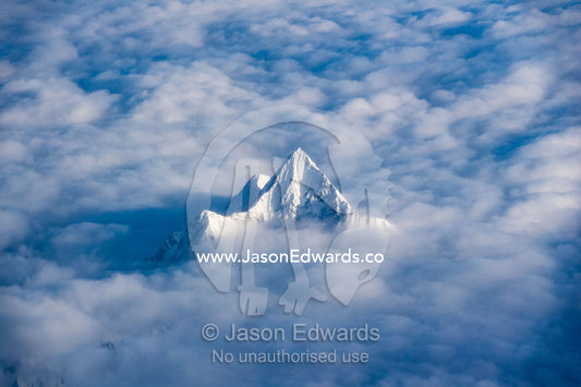 A snow and ice covered peak rises above the clouds in the Himalaya Mountains. Tibet Autonomous Region, Tibet