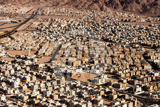 Crowded apartment blocks and housing estates fill a desert valley floor. Amman, Jordan