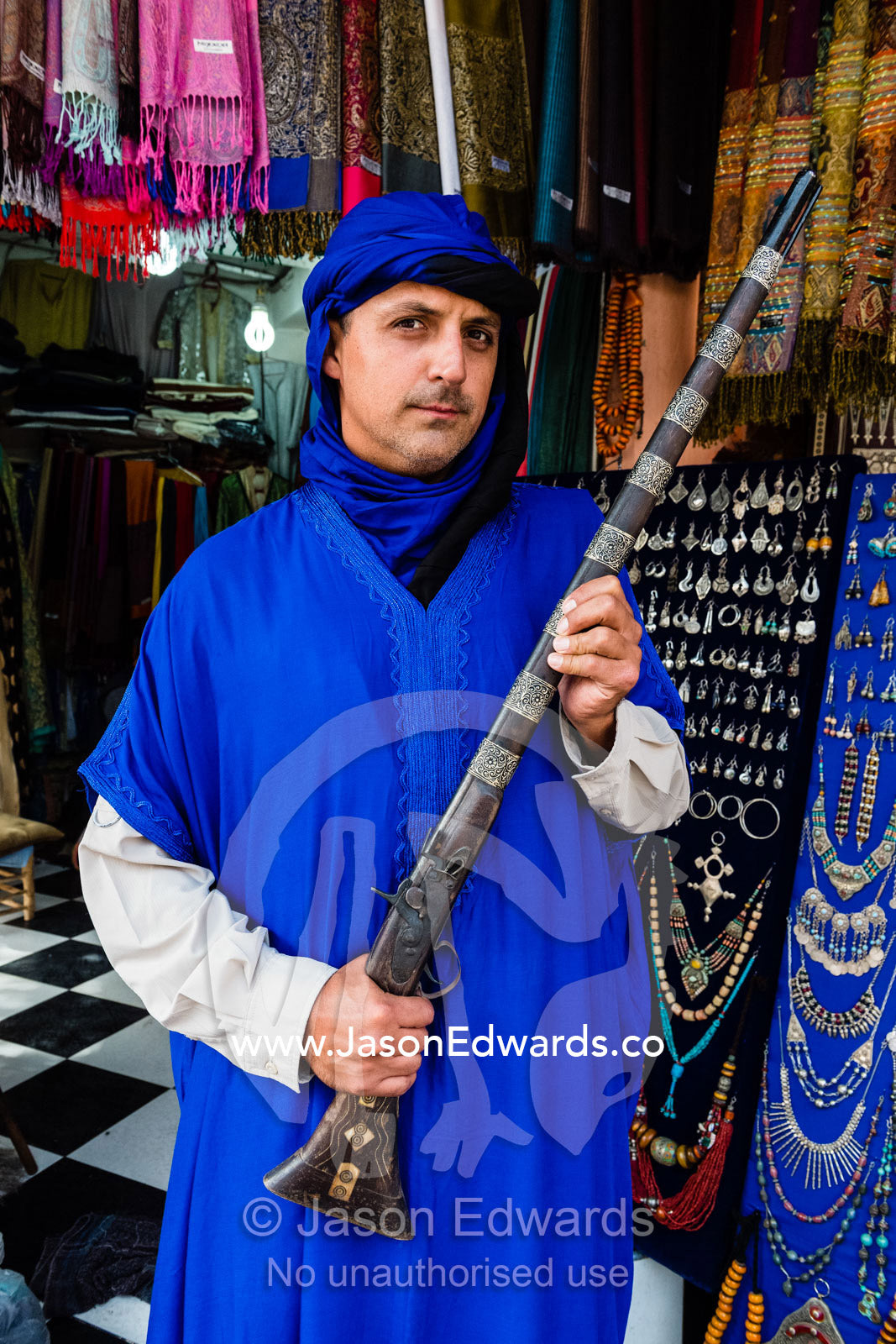 A man wearing a traditional turban and gandoura holding an antique rifle. Marrakech, Marrakech Souk, Medina of Marrak, Morocco