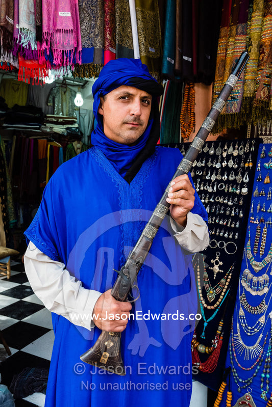 A man wearing a traditional turban and gandoura holding an antique rifle. Marrakech, Marrakech Souk, Medina of Marrak, Morocco