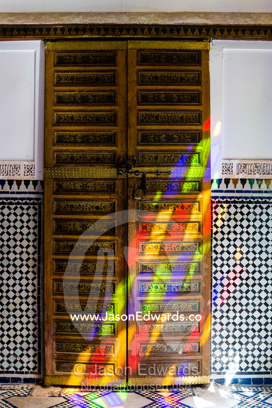 Colorful sunlight patterns through a stained glass window fall on a wooden door in a palace. Marrakech, Bahia Palace, Morocco