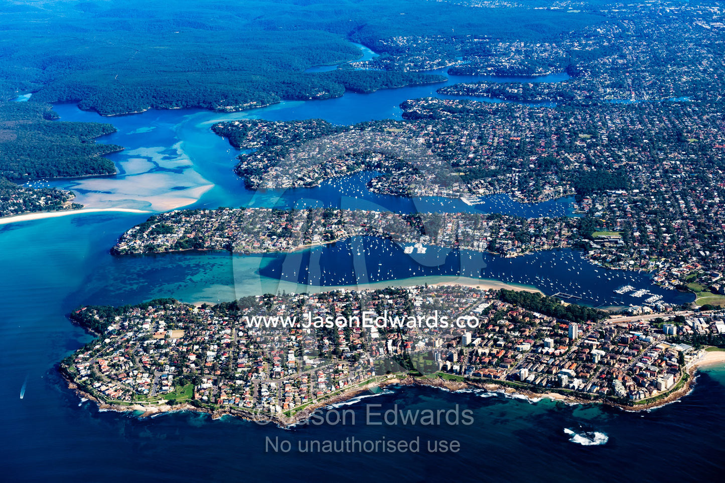 An aerial view of houses crammed together in suburbs along a coastline and river estuary. Sydney, New South Wales, Australia