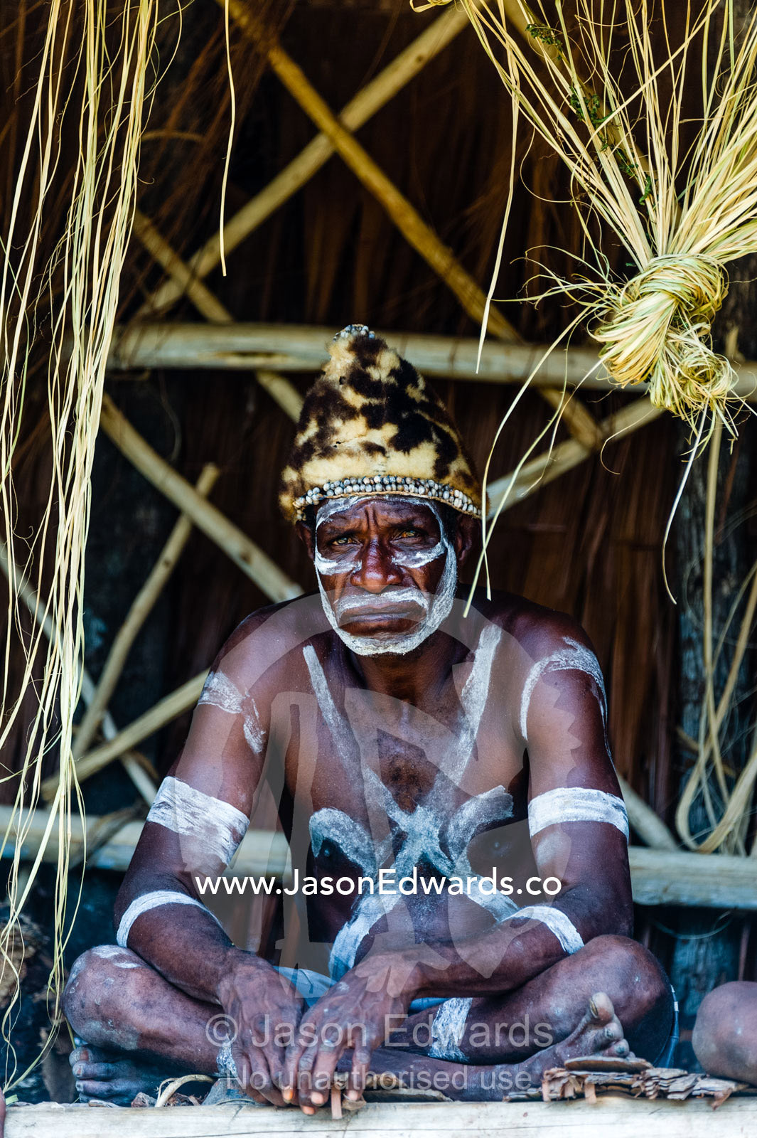 An Asmat warrior in war paint wearing a hat made of Spotted Cuscus fur. Syuru Village, Asmat Regency, Papua, Indonesia