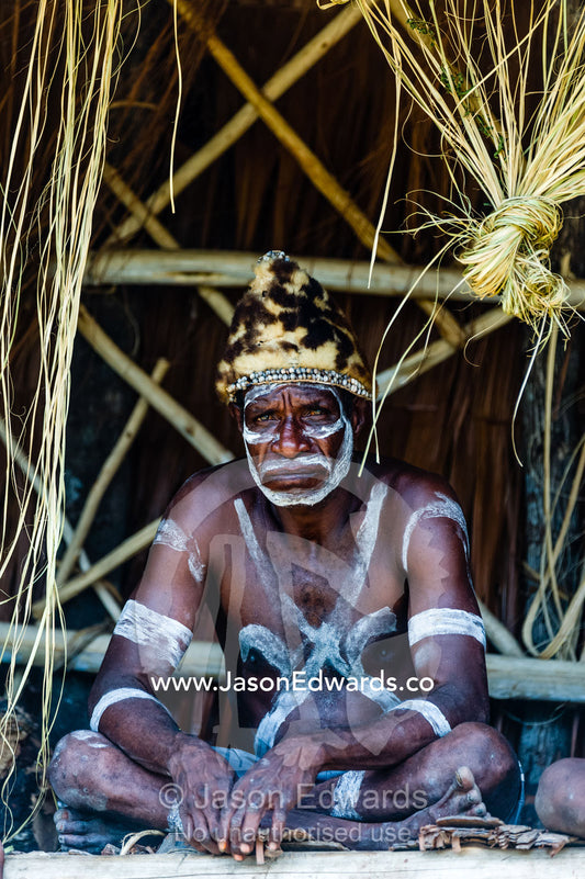 An Asmat warrior in war paint wearing a hat made of Spotted Cuscus fur. Syuru Village, Asmat Regency, Papua, Indonesia