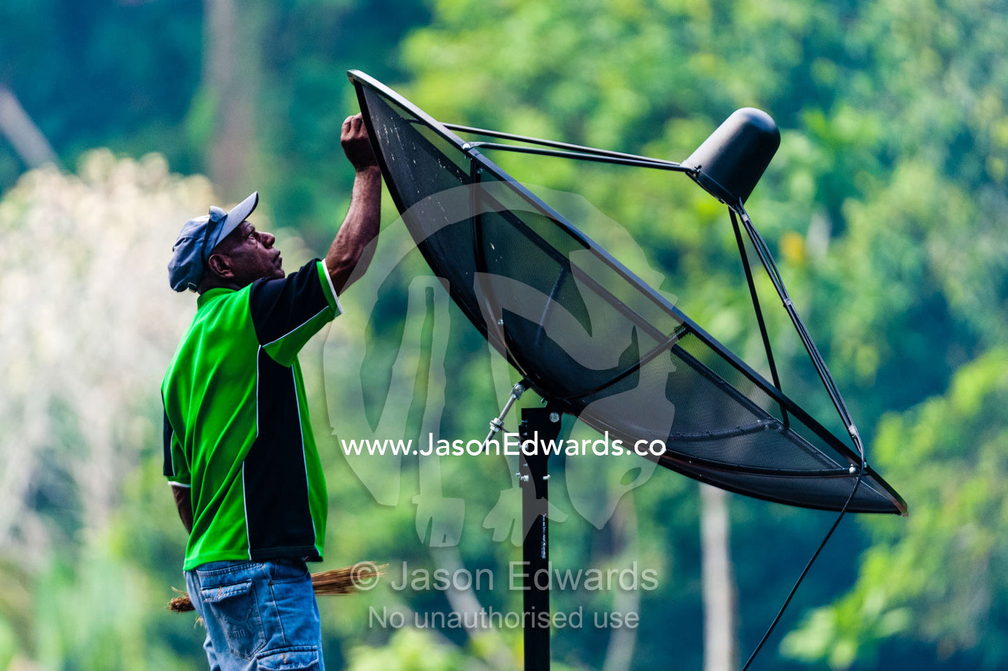 A man cleaning his home satellite dish on a remote tropical island. Samarai Island, Orangerie Bay, Milne Bay Province, Papua New Guinea