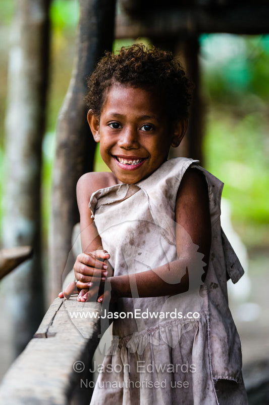 A smiling young girl in a torn dress resting on a handrail. Fergusson Island D'Entrecasteaux, Milne Bay Province, Papua New Guinea